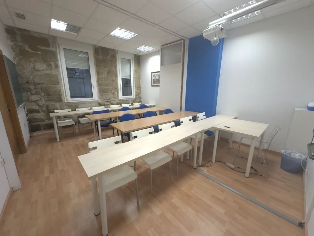 Aula grande con muro de piedra, mesas en filas y proyector