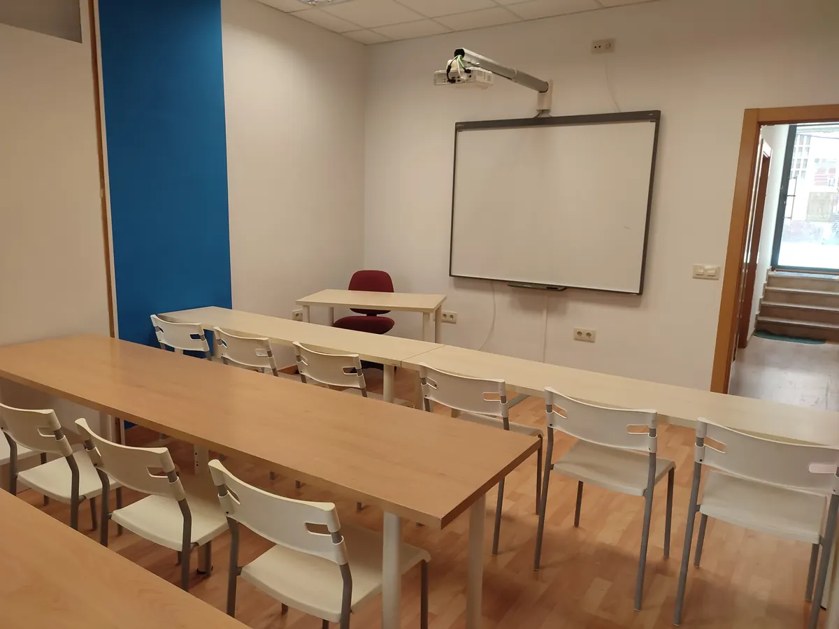 Aula con mesas de madera y pizarra digital al fondo