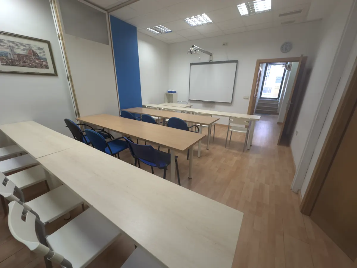 El aula con mesas y sillas en filas, proyector y pizarra digital